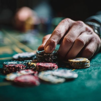 A close-up, vibrant photo of a person's hands placing casino chips onto a green felt table during a poker game.